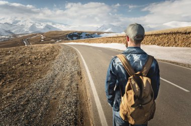 Sakallı bir adam uzun bir yol gitmek için hazır bir sırt çantası ile bir kap içinde. Dağlar ve bulutlar fon karşı bir ülke yolda bir adam