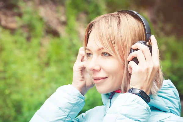 Müzik açık havada ormandaki kulaklık tutan güzel bir genç kadın portresi kapatın. Neşeli müzik