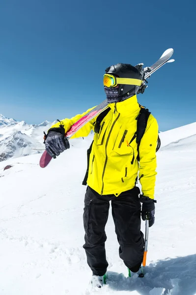 Een portret van een skiër in een beschermende helm en bril is een masker en een sjaal met ski's op zijn schouder in de besneeuwde bergen van de Kaukasus. Skiën, — Stockfoto