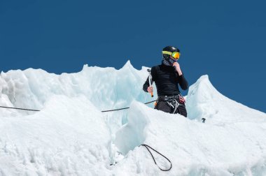 Profesyonel dağcı bir kask ve kar maskesi sigortası buzul buz AX'te çentik. Profesyonel dağcı çalışmalarında kış mavi gökyüzüne karşı bir buzulun üzerinde