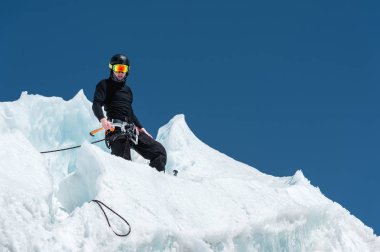 Profesyonel dağcı bir kask ve kar maskesi sigortası buzul buz AX'te çentik. Profesyonel dağcı çalışmalarında kış mavi gökyüzüne karşı bir buzulun üzerinde