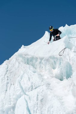 Profesyonel dağcı bir kask ve kar maskesi sigortası buzul buz AX'te çentik. Profesyonel dağcı çalışmalarında kış mavi gökyüzüne karşı bir buzulun üzerinde