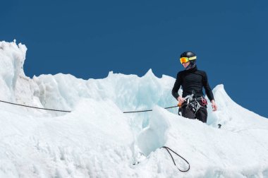 Profesyonel dağcı bir kask ve kar maskesi sigortası buzul buz AX'te çentik. Profesyonel dağcı çalışmalarında kış mavi gökyüzüne karşı bir buzulun üzerinde