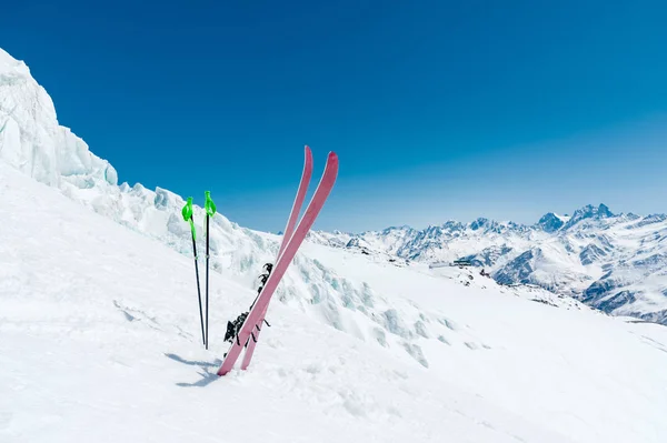 Ett par skidor och skidstavar sticka ut i snön på Kaukasus mot bakgrund av bergskedjan kaukasiska berget sluttning och den blå himlen på en solig dag — Stockfoto