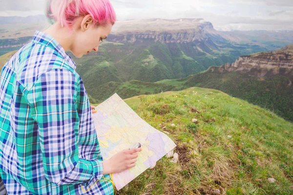 Viajante menina com cabelo multi-colorido sentado no cartão de leitura da natureza e segurando uma bússola na mão. O conceito de navegação na busca e turismo nas montanhas. Conceito de viagem — Fotografia de Stock