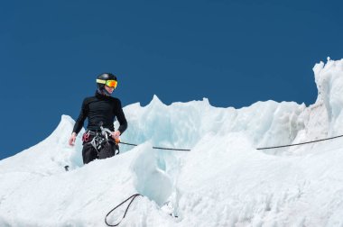 Profesyonel dağcı bir kask ve kar maskesi sigortası buzul buz AX'te çentik. Profesyonel dağcı çalışmalarında kış mavi gökyüzüne karşı bir buzulun üzerinde