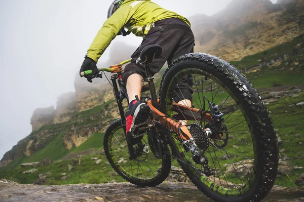 Gambe del ciclista e ruota posteriore primo piano vista della bici mtb posteriore in montagna sullo sfondo di rocce in tempo nebbioso. Il concetto di sport estremi — Foto Stock