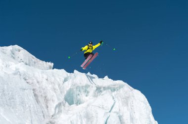 Bir mavi gök yüksek dağlarda karşı bir buzul üzerinden atlama atlama bir kayakçı. Profesyonel kayak