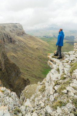 bir rock kenarında duran ve destansı bir plato üzerinde mesafe içine bakan sakallı hippi turist adam. Turizm kavramı
