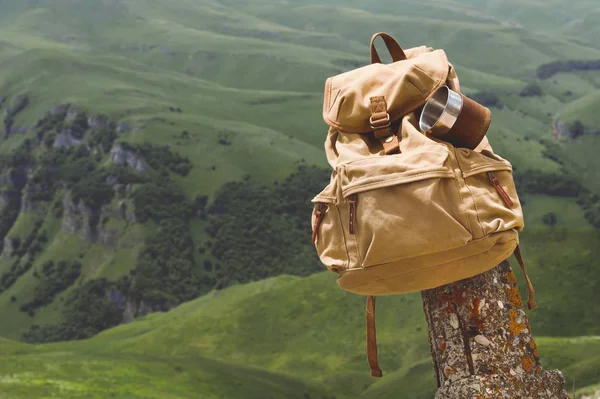 Hipster yellow vintage backpack with a mug fixed on it with a mug close-up front view. Travelers travel bag in the background of a mountain landscape — Stock Photo, Image