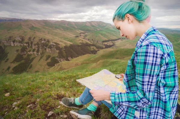 Viajante menina com cabelo multi-colorido sentado no cartão de leitura da natureza e segurando uma bússola na mão. O conceito de navegação na busca e turismo nas montanhas. Conceito de viagem — Fotografia de Stock