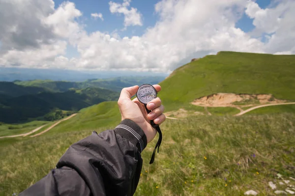 Mano de un turista con una brújula auténtica en el fondo de un paisaje de carretera de montaña — Foto de Stock