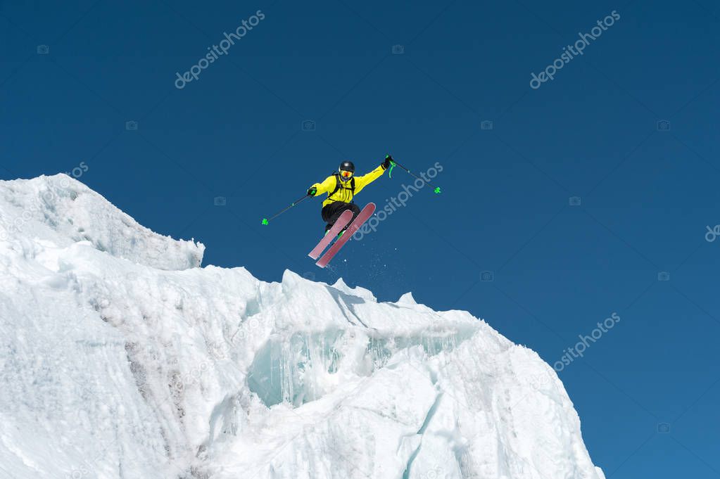 A jumping skier jumping from a glacier against a blue sky high in the mountains. Professional skiing