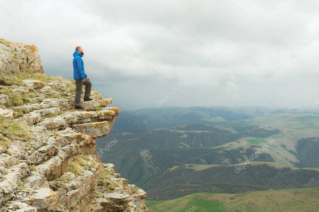 bearded hipster tourist man standing on the edge of a rock and looking out into the distance on an epic plateau. The concept of tourism