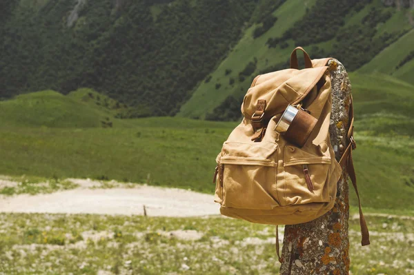 Hipster sarı vintage sırt çantası üzerinde bir kupa yakın çekim önden görünüm ile sabit bir kupa ile. Travelers seyahat çantası bir dağ manzarası arka planda