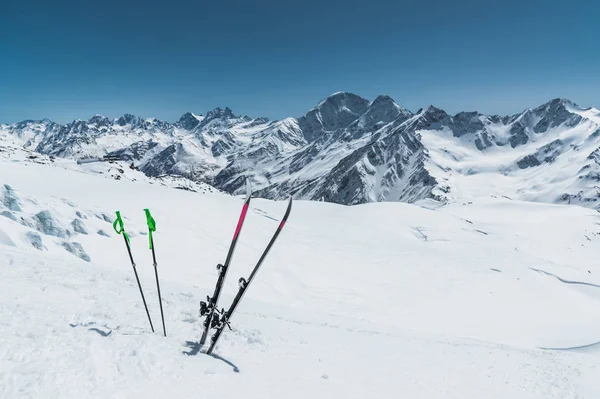 Een paar ski's en skistokken uit stok in de sneeuw op de berghelling van de Kaukasus tegen de achtergrond van de Kaukasische bergketen en de blauwe hemel op een zonnige dag — Stockfoto