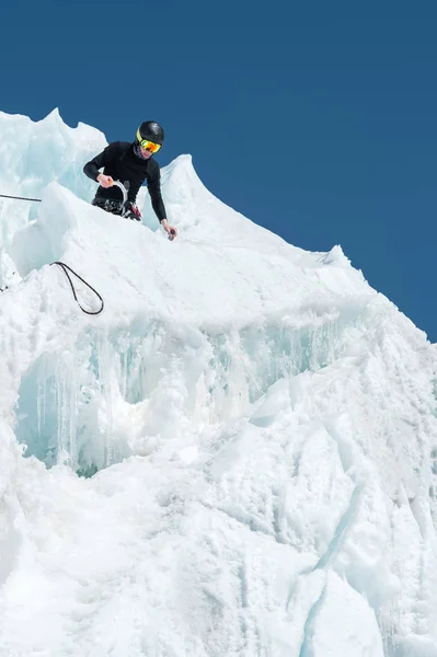 Een professionele bergbeklimmer in een helm en ski-masker op de verzekering het ijs ax in de gletsjer notch. Het werk van een professionele klimmer in de winter op een gletsjer tegen de blauwe hemel — Stockfoto