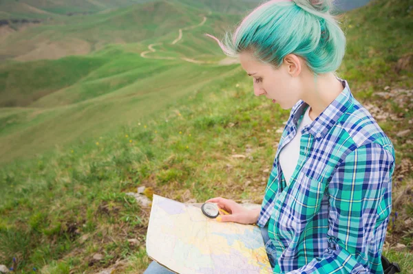 Viajante menina com cabelo multi-colorido sentado no cartão de leitura da natureza e segurando uma bússola na mão. O conceito de navegação na busca e turismo nas montanhas. Conceito de viagem — Fotografia de Stock