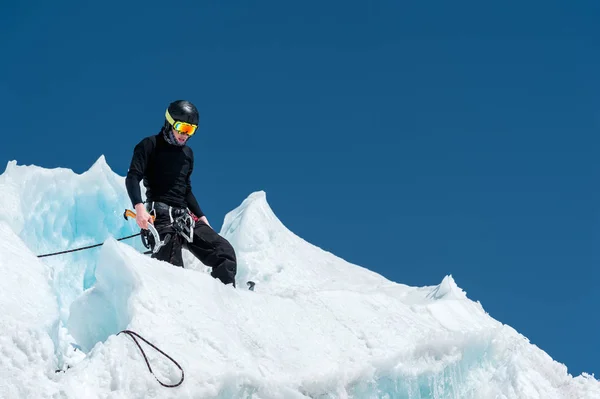 Επαγγελματία ορειβάτη σε ένα κράνος και τη μάσκα του σκι για την ασφάλιση εγκοπή το ax πάγο στον παγετώνα. Το έργο του μια επαγγελματική αναρρίχηση το χειμώνα σε έναν παγετώνα ενάντια στον γαλάζιο ουρανό — Φωτογραφία Αρχείου
