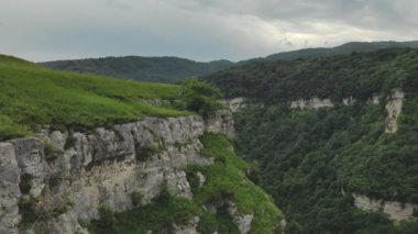 Genç hipster kadın rock uzun duvar çimenlerin üzerinde kenarında oturuyor. Havadan görünümü. Uçak modeli için yavaş ileri uçuyor. İfşa atış kurulması