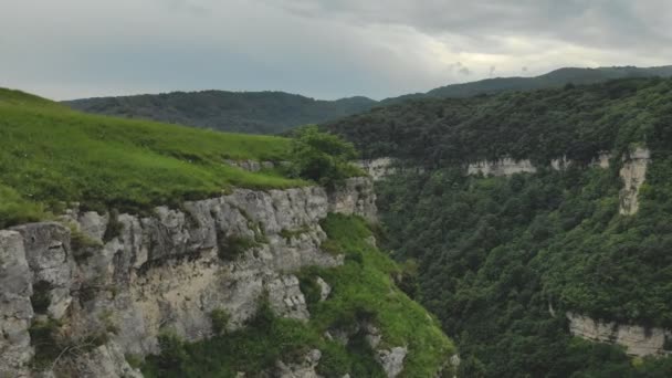 Mujer hipster joven está sentado en el borde en la hierba de la pared alta de roca. Vista aérea. Drone está avanzando lentamente hacia el modelo. Establecimiento de tiro revelador — Vídeos de Stock