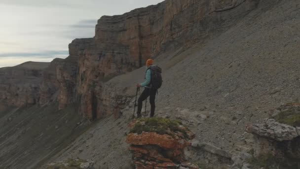 Aérea: vuelo de regreso de una mujer adulta joven con una mochila que llega a la cima de la roca al pie de la épica meseta al atardecer. Vista desde atrás. Rusia. Cáucaso Norte — Vídeo de stock