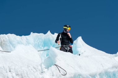 Profesyonel dağcı bir kask ve kar maskesi sigortası buzul buz AX'te çentik. Profesyonel dağcı çalışmalarında kış mavi gökyüzüne karşı bir buzulun üzerinde
