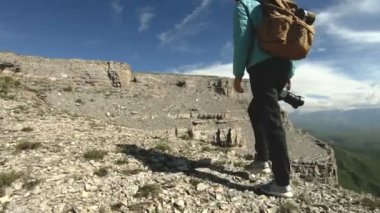 Arkadan şapkalı bir kız gidiyor fotoğrafçı tür. Bir turist fotoğrafçı ile bir sırt çantası ve elinde bir fotoğraf makinesi görünümü hayran uçurumun kayalıkbir platonun yürüyor. Yavaş