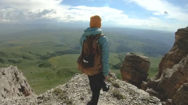 Een lachende reiziger meisje met een rugzak en zonnebril loopt met haar camera op de rand van een rotsachtig plateau in de Kaukasus — Stockvideo