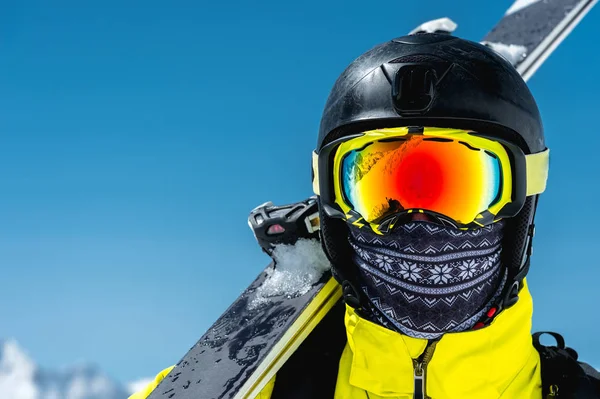 Um grande retrato de um esquiador em um capacete protetor e óculos - uma máscara e um lenço ao lado dos esquis contra as montanhas cobertas de neve do Cáucaso. Esqui — Fotografia de Stock