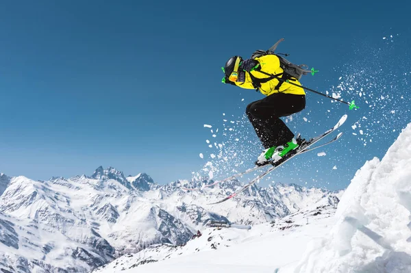 En skidåkare i full sport utrustning hoppar in i branten från toppen av glaciären mot bakgrund av den blå himlen och de kaukasiska snöklädda bergen. Elbrus regionen. Ryssland — Stockfoto