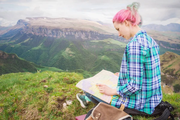 Viajante menina com cabelo multi-colorido sentado no cartão de leitura da natureza e segurando uma bússola na mão. O conceito de navegação na busca e turismo nas montanhas. Conceito de viagem — Fotografia de Stock