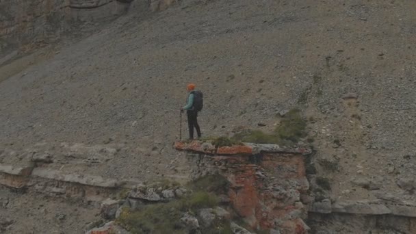 Aerial - volo intorno a una giovane donna adulta con uno zaino che raggiunge la cima della roccia ai piedi dell'epico altopiano al tramonto. Vista dal retro. Russia. Caucaso settentrionale — Video Stock