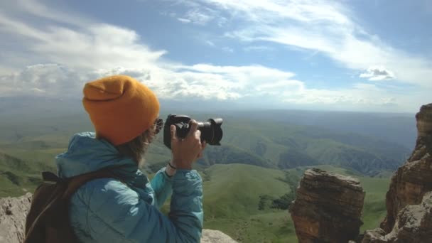 戴着帽子的金发女郎摄影师在她的数码相机上拍了一张照片 上面有高加索的岩石背景 — 图库视频影像