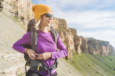 Güneş gözlüklü bir turist epik kaya tırmanışı ile doğa yürüyüşü için hazırlanıyor arka plan üzerinde doğada bir sırt çantası koyar. Kız uzun yürüyüşe çıkan kimse bağlantı elemanları üzerinde sırt çantası takılır..