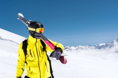 Bir yamaçta ayakta kayakçı. Biri hafif bir takım, kask ve maske içinde kayak kayak yapmak. Arka plan karla kaplı dağlara, kayakçı. Kafkas Dağları, Elbrus, Rusya Federasyonu