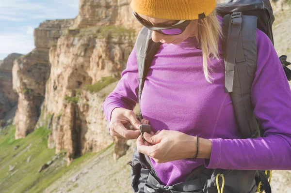 Egy turista napszemüveg egy hátizsák helyezi a természet a háttérben a felkészülés trekking hegymászás epikus sziklák. A lány természetjáró rögzíti a rögzítőelemeket a hátizsák — Stock Fotó