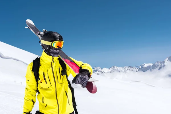 Skidåkare står i en sluttning. Mannen i en ljus kostym, hjälm och mask i skidåkning är att åka skidor. I bakgrunden snöklädda bergen, skidåkare. Kaukasus, Elbrus, Ryssland — Stockfoto