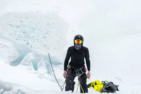 Um montanhista profissional em um capacete e máscara de esqui no seguro não entalhe o machado de gelo na geleira. O trabalho de um alpinista profissional no inverno em uma geleira contra o céu azul — Fotografia de Stock