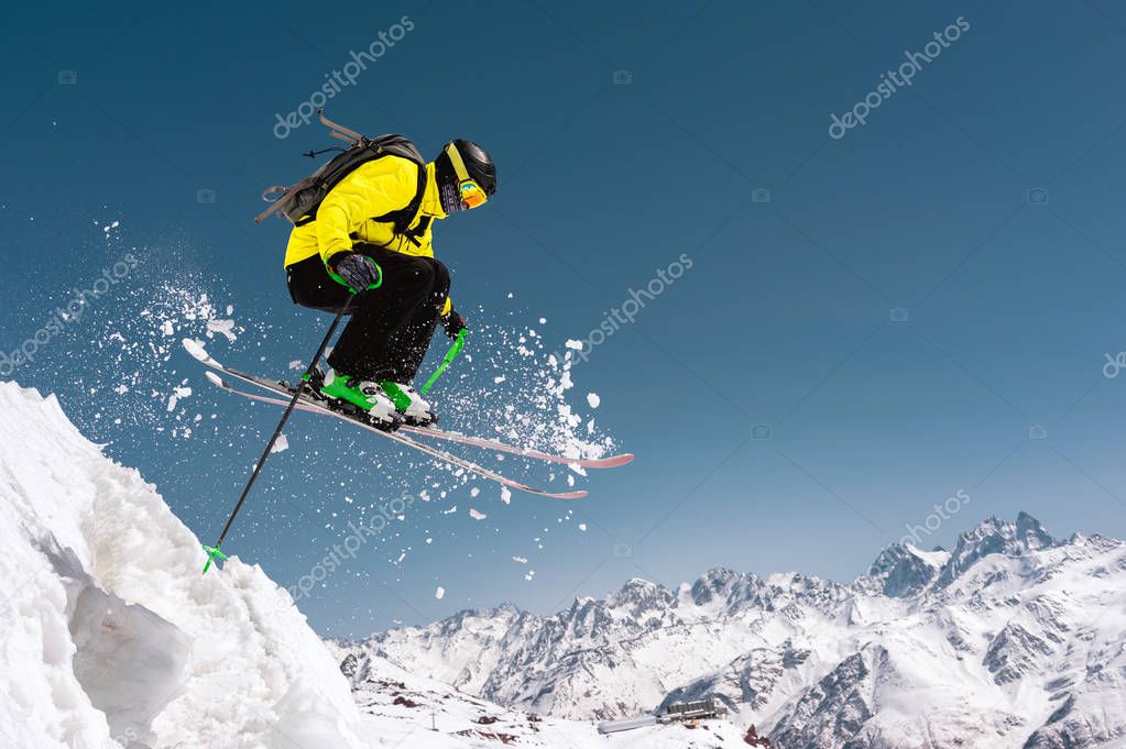 A skier in full sports equipment jumps into the precipice from the top of the glacier against the background of the blue sky and the Caucasian snow-capped mountains. Elbrus region. Russia