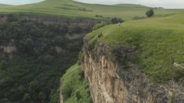 Gözlük ve şapka kız fotoğrafçı Yaylası yakınlarında uçurumun kenarına onun dslr fotoğraf makinesi ile yürür. Havadan görünümü