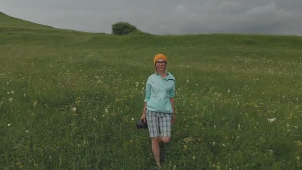 De fotograaf meisje in glazen en een hoed loopt met haar dslr camera aan de rand van het plateau in de buurt van de afgrond. Luchtfoto — Stockvideo