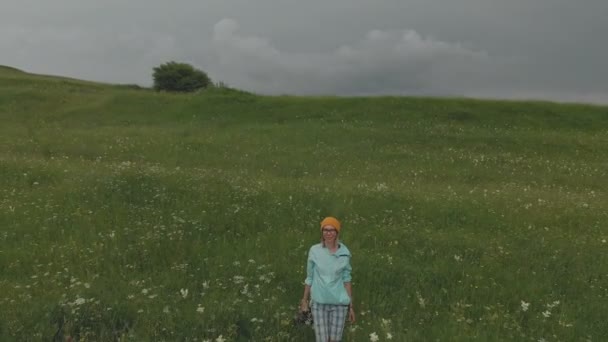 Девушка-фотограф в очках и шляпе гуляет со своей камерой dslr на краю плато возле пропасти. Вид с воздуха — стоковое видео