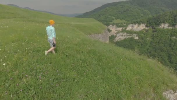 De fotograaf meisje in glazen en een hoed loopt met haar dslr camera aan de rand van het plateau in de buurt van de afgrond. Luchtfoto — Stockvideo