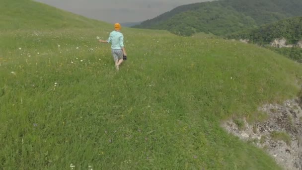 Die Fotografin mit Brille und Hut geht mit ihrer DSLR-Kamera am Rand des Plateaus in der Nähe des Abgrunds. Luftbild — Stockvideo