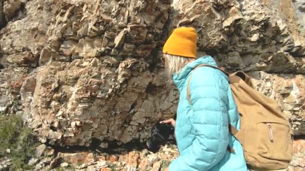 Chica rubia fotógrafa en la gorra toma una foto en su cámara digital con un fondo de rocas en el Cáucaso — Vídeo de stock