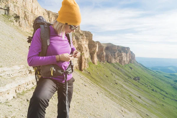 Egy turista napszemüveg egy hátizsák helyezi a természet a háttérben a felkészülés trekking hegymászás epikus sziklák. A lány természetjáró rögzíti a rögzítőelemeket a hátizsák — Stock Fotó