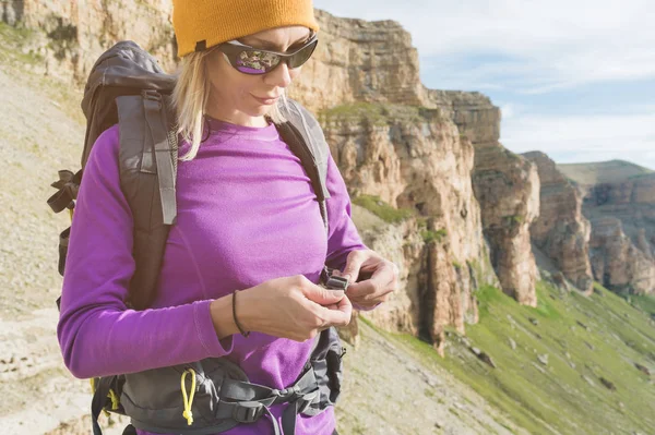 Egy turista napszemüveg egy hátizsák helyezi a természet a háttérben a felkészülés trekking hegymászás epikus sziklák. A lány természetjáró rögzíti a rögzítőelemeket a hátizsák — Stock Fotó