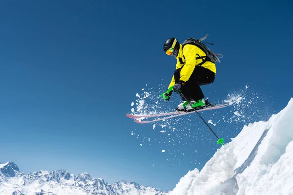 Un skieur en équipement sportif complet saute dans le précipice depuis le sommet du glacier sur fond de ciel bleu et de montagnes enneigées du Caucase. Région d'Elbe. Russie — Photo