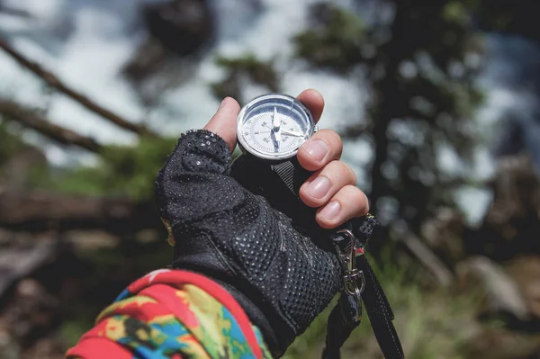 Ruka drží magnetický kompas na pozadí jehličnatého lesa a horské řeky. Koncept outdoor navigace — Stock fotografie